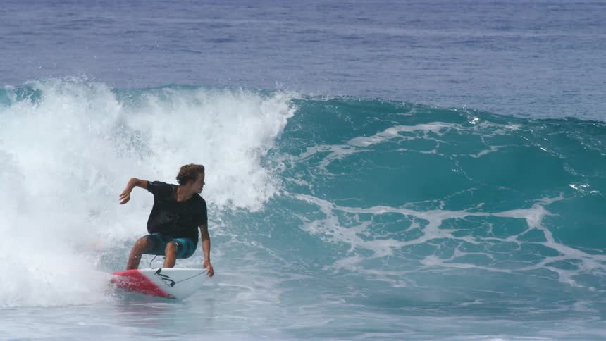 Young man rides a red and white surfboard over the ocean waves
