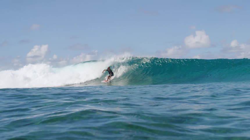 A surfer wearing shorts and a t shirt rides a big wave