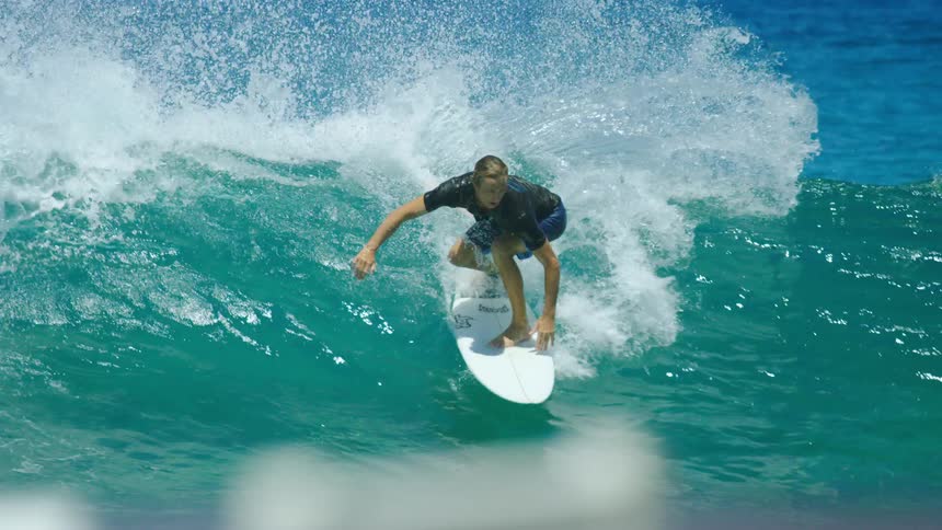 Male surfer with black shirt and blue shorts rides on ocean wave