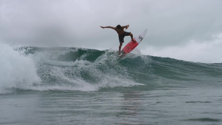 Surfer rides surfboard along wave under overcast sky