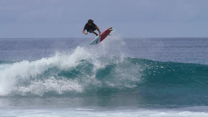 Male surfer with black t shirt and blue shorts rides on ocean wave