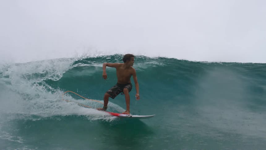 A teenage boy surfing an ocean wave during a rainstorm