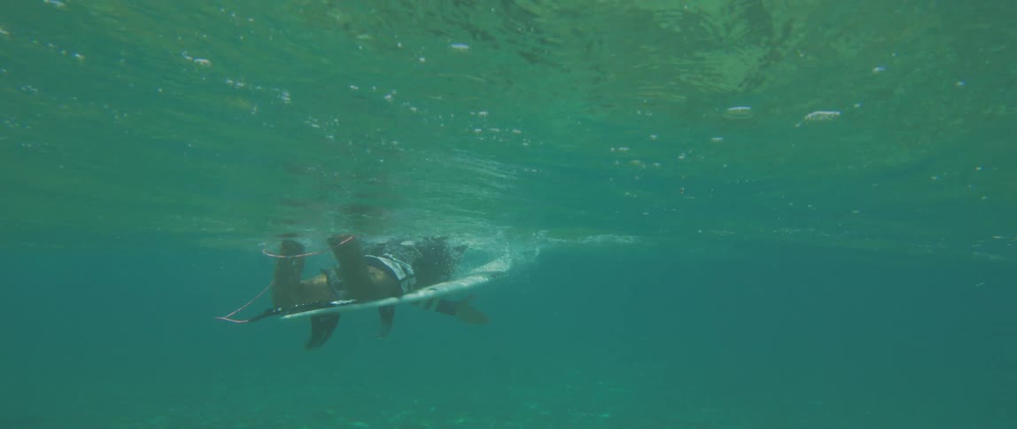 A male surfer floating on a surfboard in blue ocean water