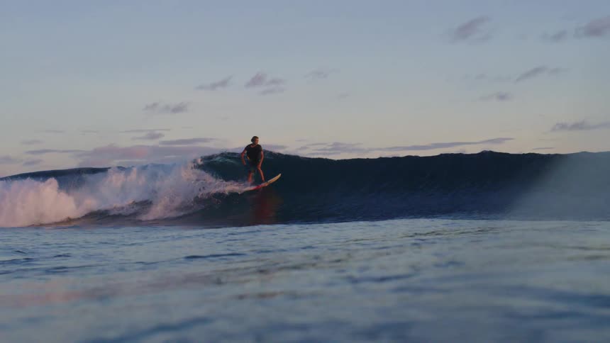 A man is surfing on ocean waves at dusk