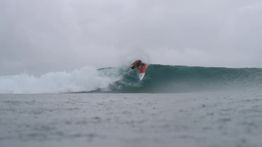 A surfer wearing dark colored shorts rides a big wave as rain falls into the water