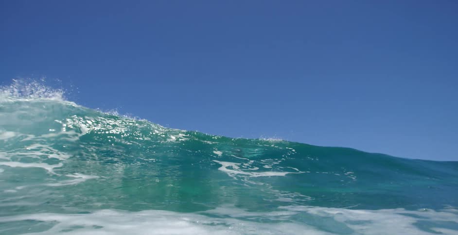A man is laying on a surfboard as a wave rolls underneath him