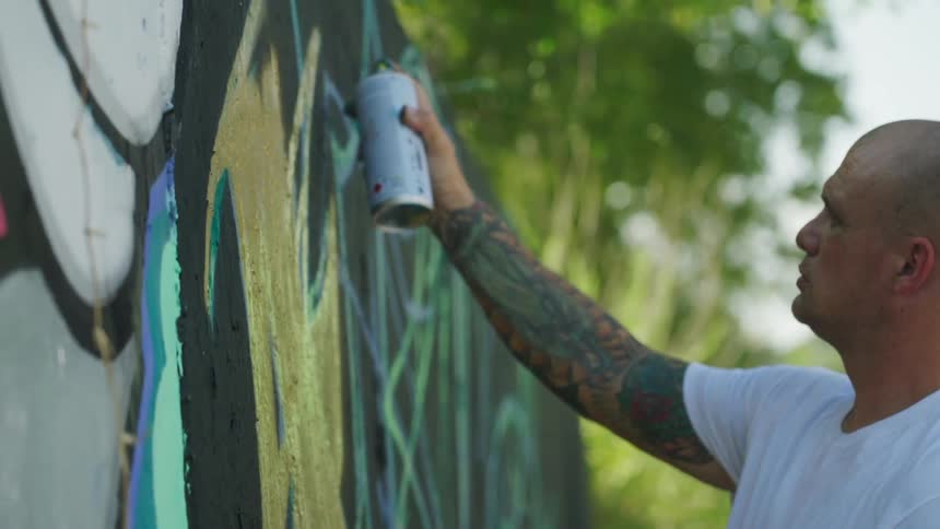 A man is outdoors and spray painting a wall