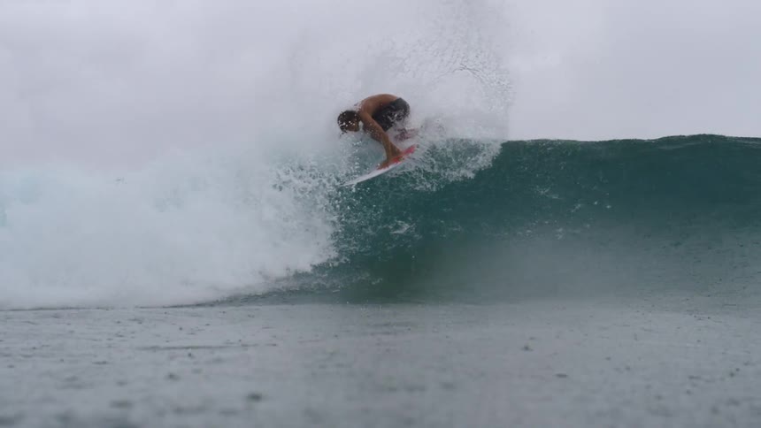 A teenage boy surfing an ocean wave during a rainstorm
