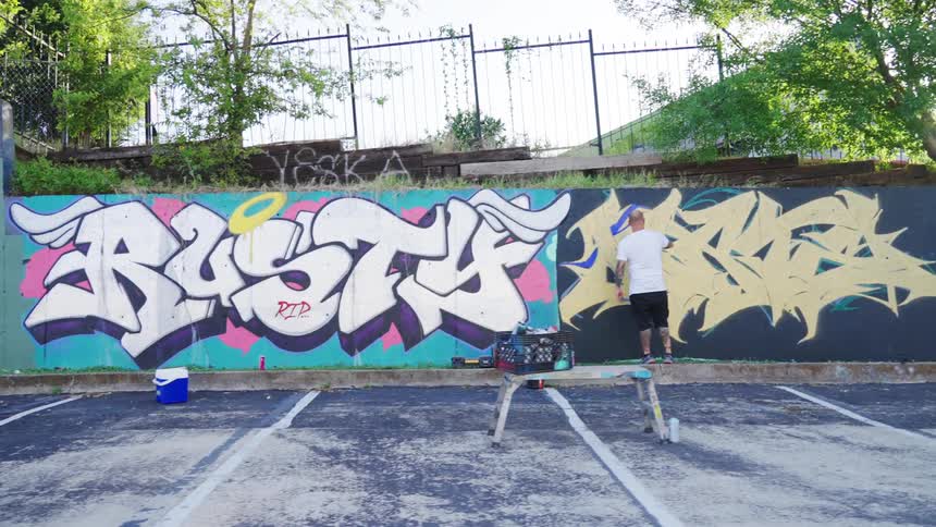 A man spray painting graffiti onto a wall in a parking lot in the daytime
