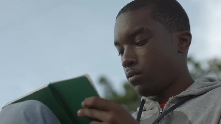 A man is sitting down writing in a book