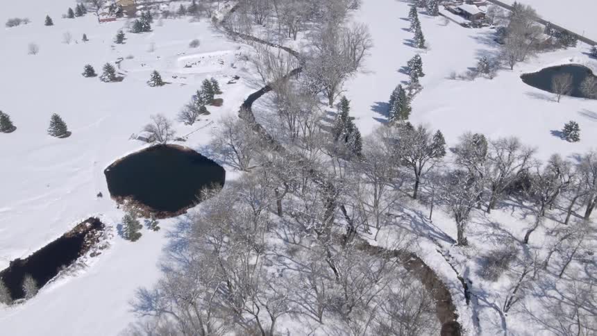 River winds past ponds and a farm and through leafless trees in winter