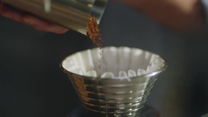 Person pours ground coffee into paper lined cup