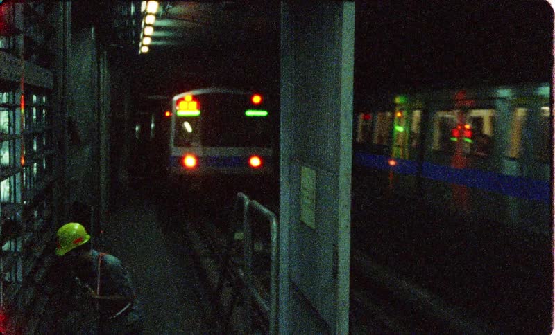 Subway worker works near track as passengers ride passing subway trains