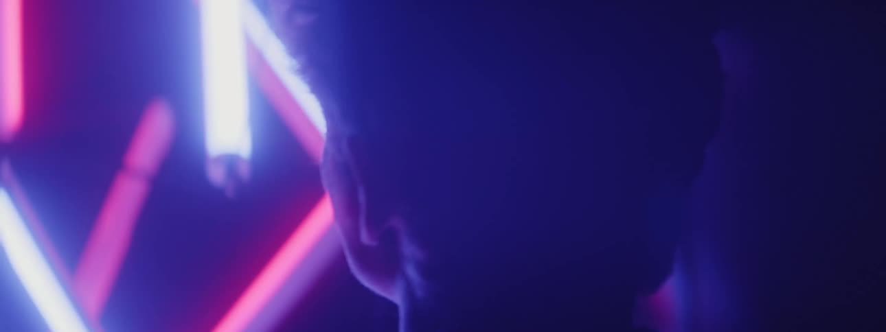 A man walks past neon lights in the dark