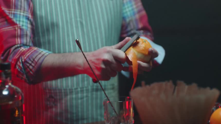A man in a striped apron peeling an orange in a kitchen