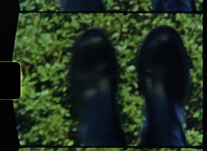 Vintage footage of a teenage girl lying on her back outdoors with her feet in the air kicking her rainboots together