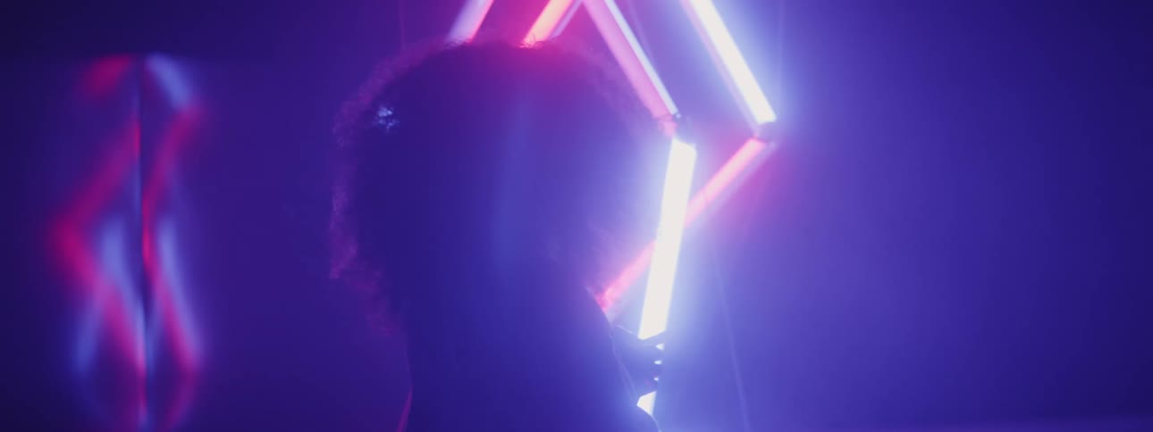 A woman walks through a room with brightly lit lights and touches one of the lights as she passes