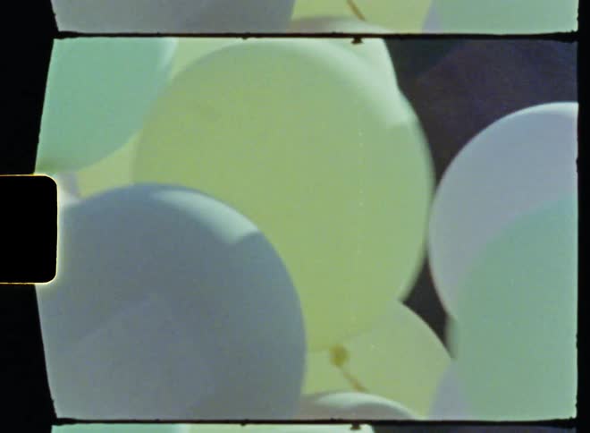 A man rides a bicycle with a bunch of balloons tied to the back along a bike path during the day