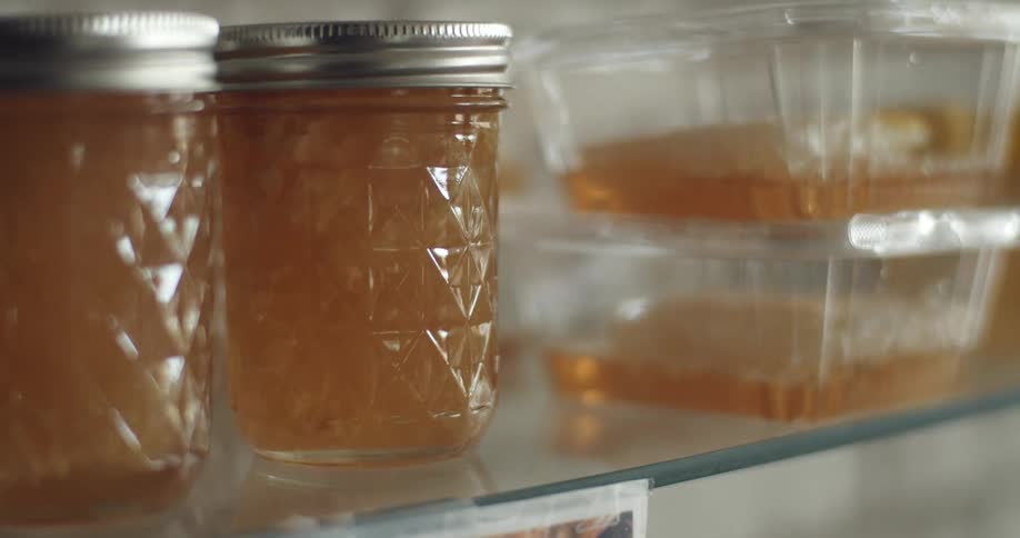 Jars and containers of honey sitting on a glass shelf