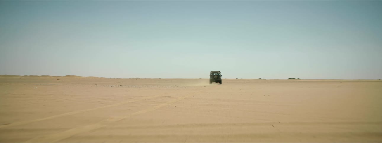 A vehicle drives across the sand in a desert