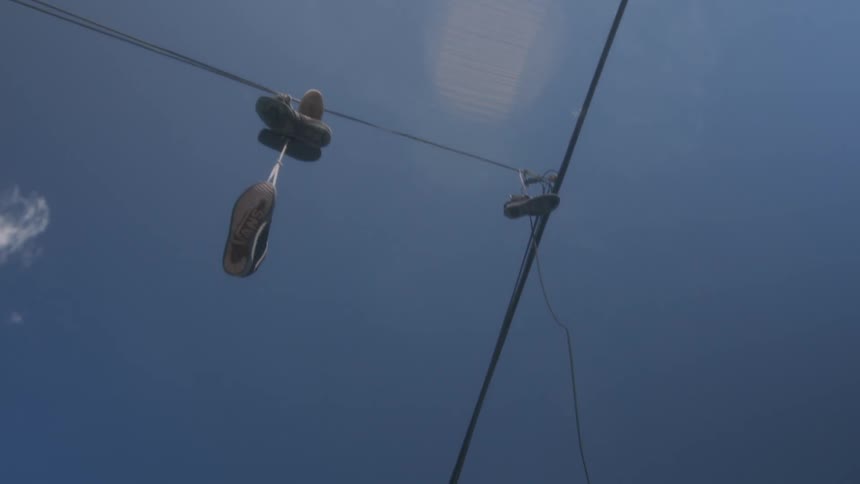 Sneakers hang from electrical wires in a clear sky