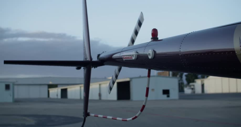 A helicopter pulls into a runway as a helicopter sits parked on a cloudy day