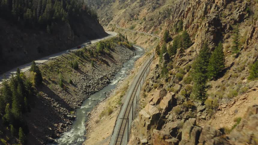 Traffic flows down highway paralleling river and train tracks near forest topped mountain side