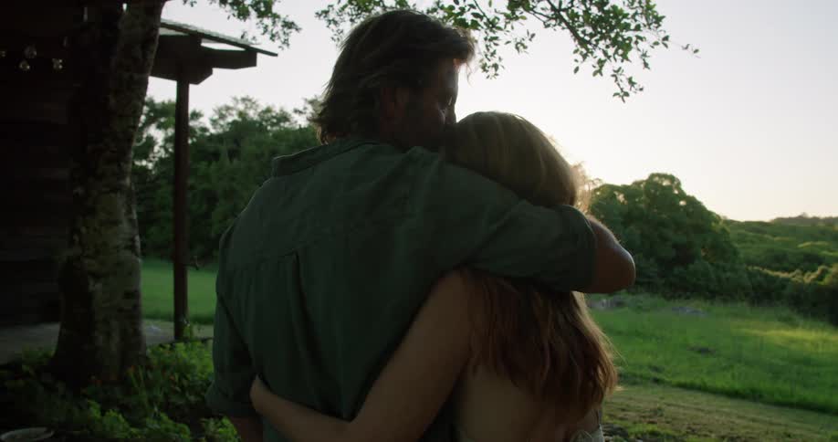 Couple hugging and kissing tenderly while looking at the sunset in the backyard