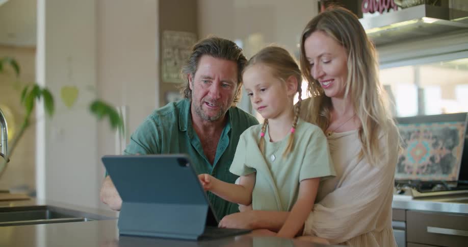 Father with beard blue shirt daughter with braids and blonde mother wearing brown dress use and look at tablet in kitchen at home