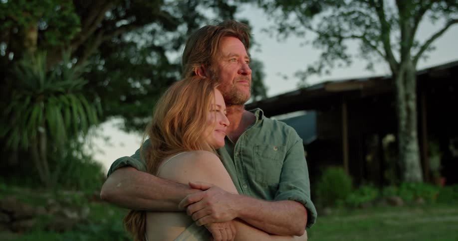 A man hugging his wife in the yard turns and kisses her forehead