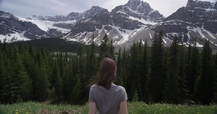A woman walks toward a forest in front of a mountain
