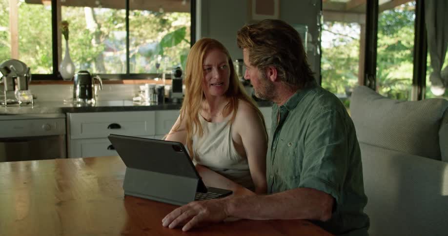 Two people are sitting in a house and looking at a laptop