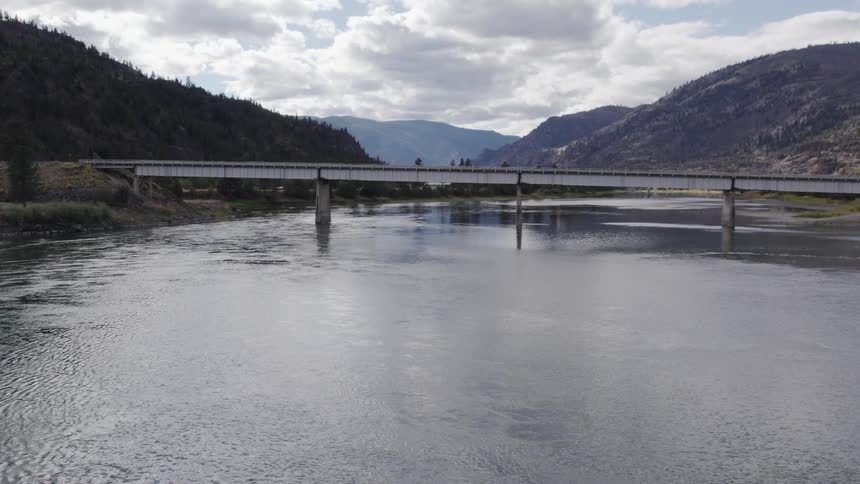 A bridge over a river with mountains in the distance under a cloudy sky
