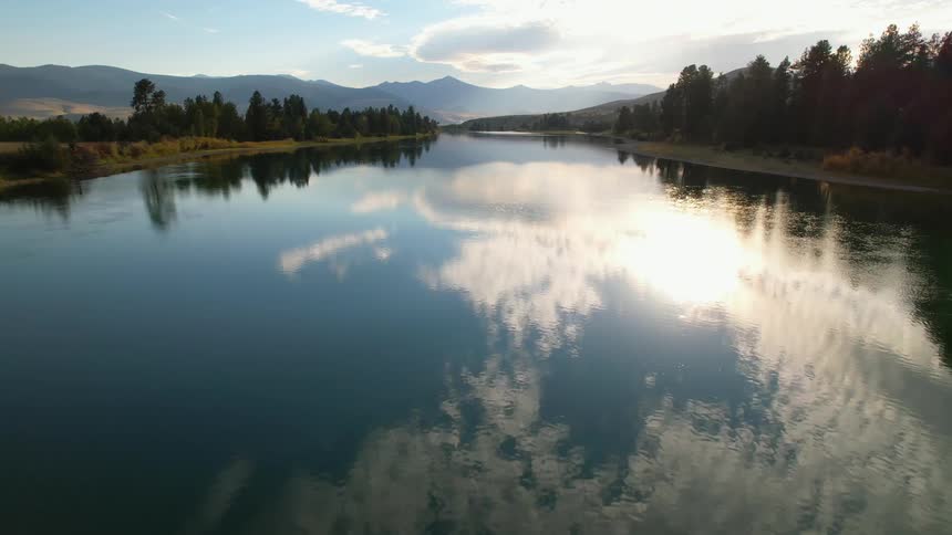 Blue skies and fluffy clouds reflect onto still lake water