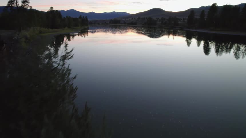 Tire tracks pass along shore of lake reflecting forest and mountains