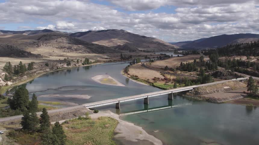 Bridge crosses river dotted with sandbars with hills and forest in the background