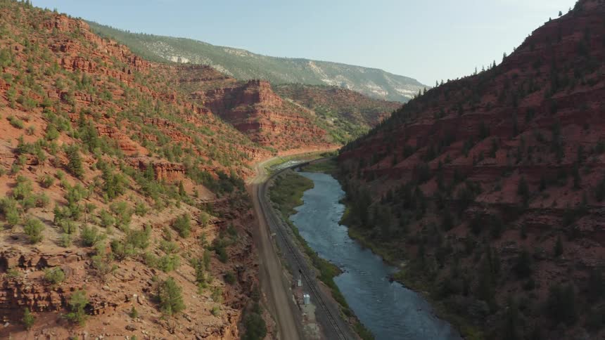 A river runs alongside a road along the bottom of a narrow valley between mountains in the badlands during the day