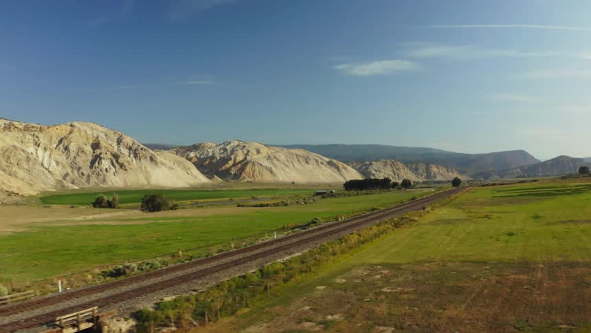 Aerial view of train tracks running in the middle of a grassland near the mountains