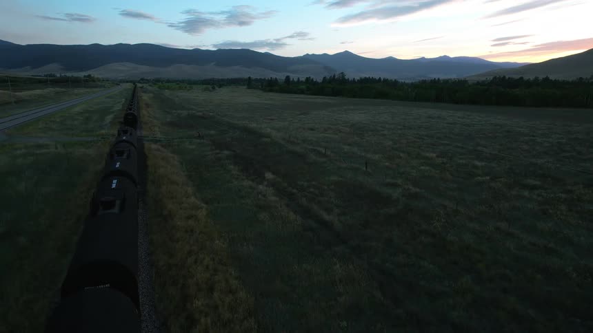 Stopped train parallels highway in grassfield leading toward mountains