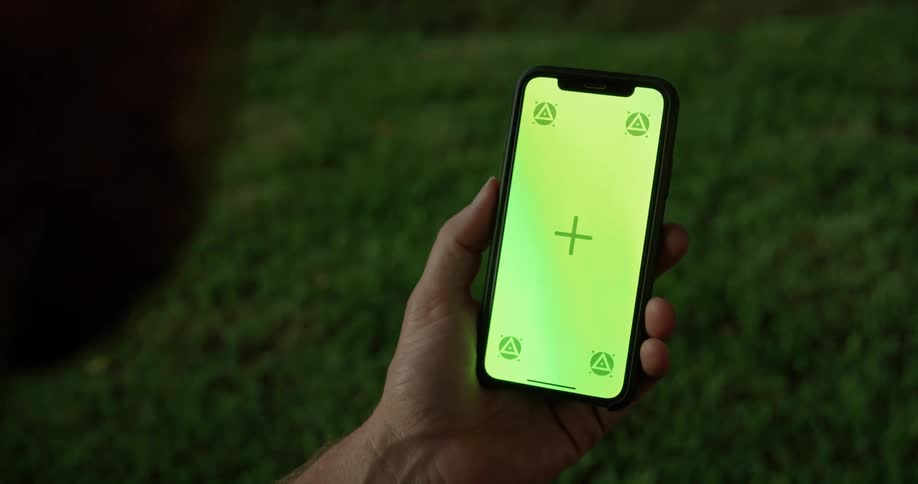 Man holding a smartphone with a green replaceable screen on his hand over green grass