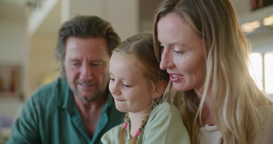 A family is sitting in the kitchen playing on a laptop