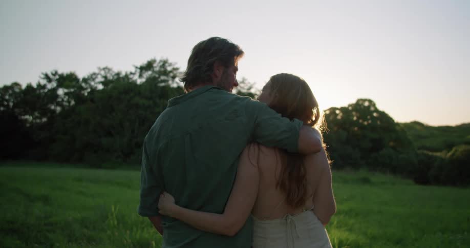 Couple hugging and kissing on a green field near the trees at sunset