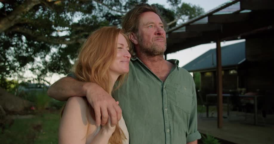 A man and a woman are standing outside and he has his arm around her and kisses her forehead