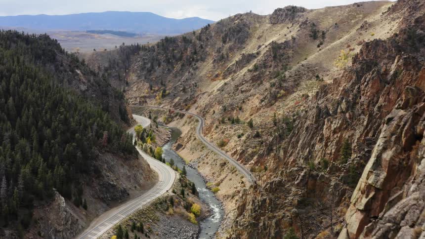 Road along the side of a forested mountain and a river below