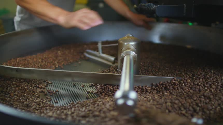 Man tossing coffee beans over a roasting machine