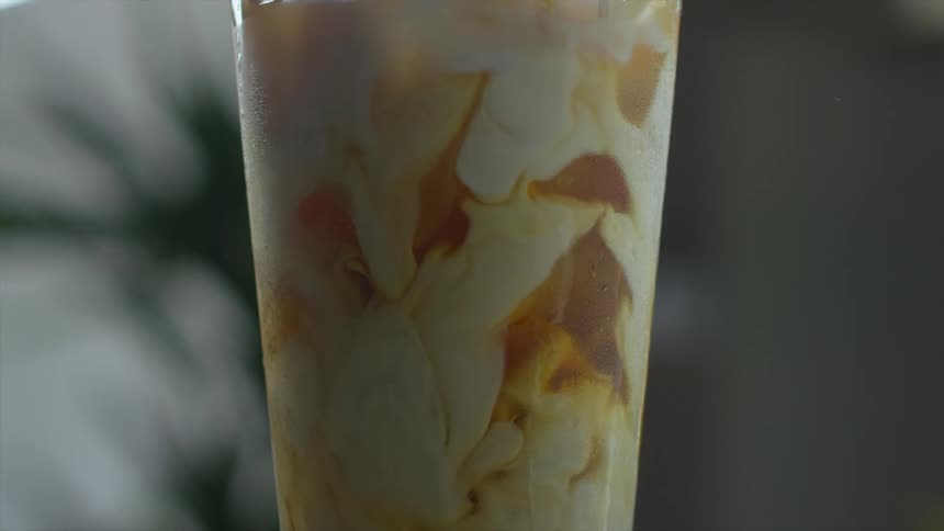 Cream is slowly poured into a pintsize glass full of an icy golden brown beverage