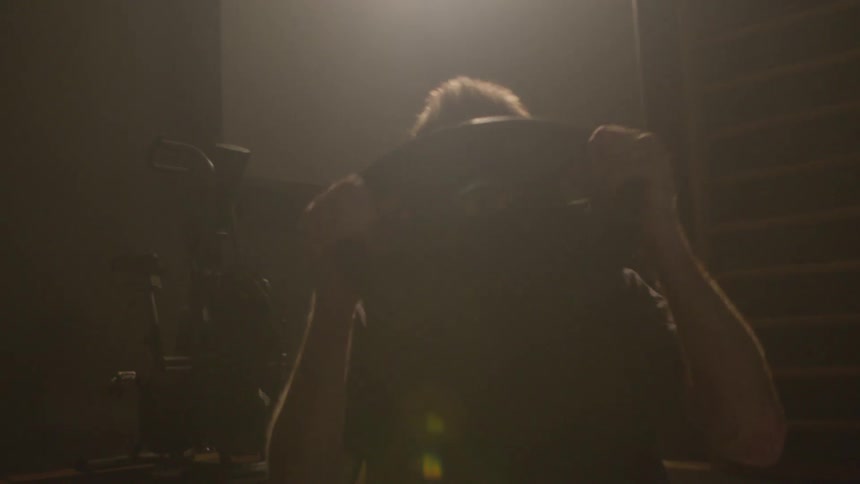 Sunlight filters through a window over a man lifting weights on a dimly lit gym at morning