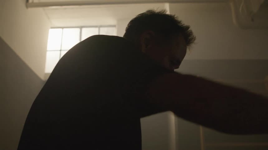 Man exercises in dim gym lit by light from high placed window