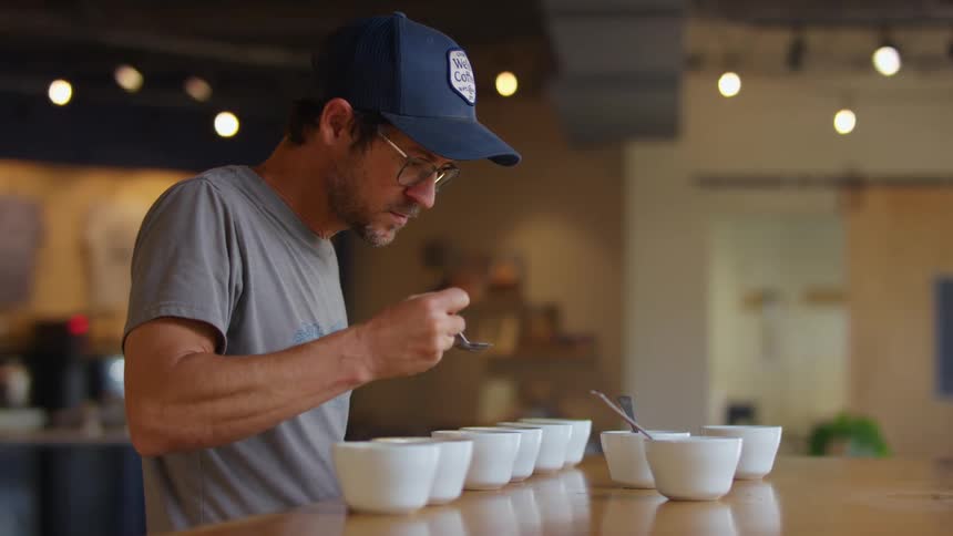 Young man wearing a baseball cap testing coffee blends on a coffee shop