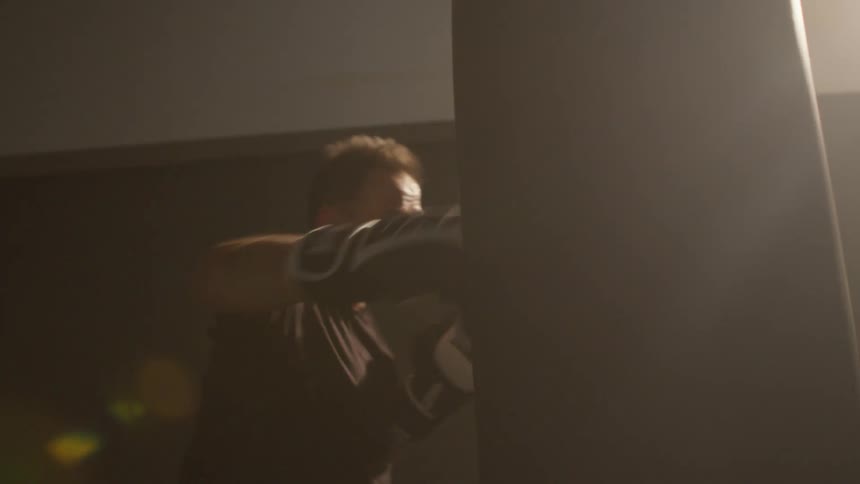 A man strikes a punching bag in a dimly lit gym during the day